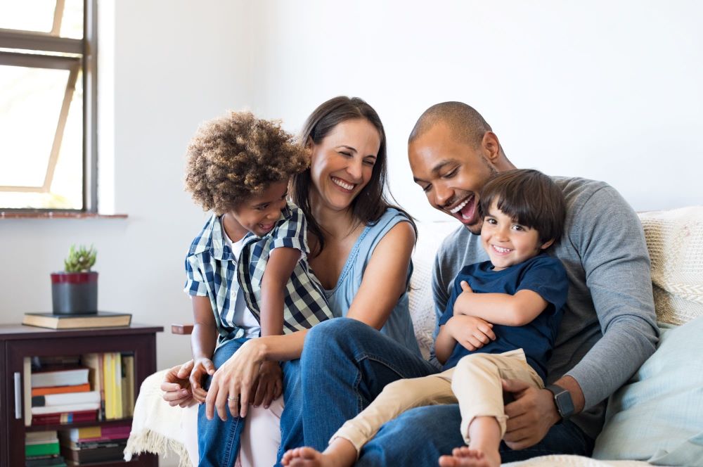 Family with 2 young children smiling sitting on a sofa